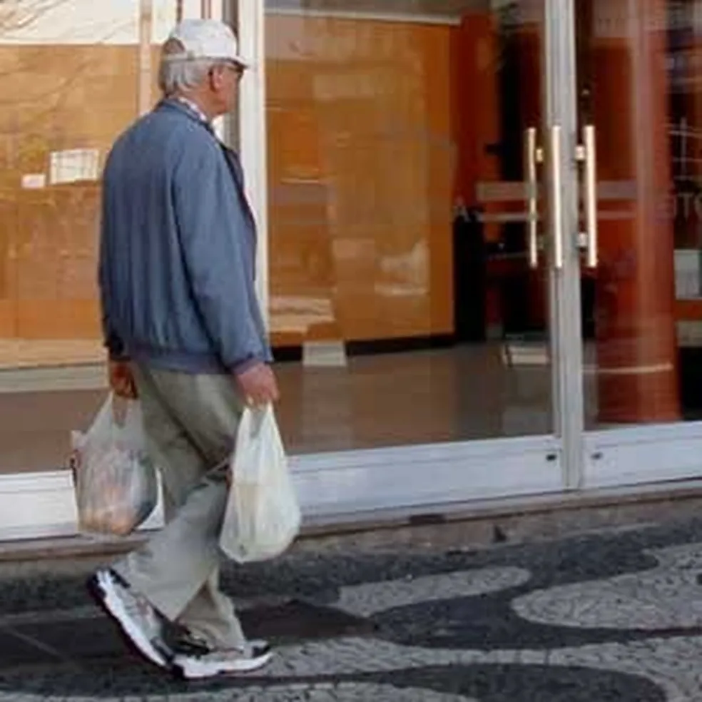 Rara foto do vampiresco Dalton Trevisan, um senhor com sacolas de compra usando boné, tênis e roupa social, no centro de Curitiba.